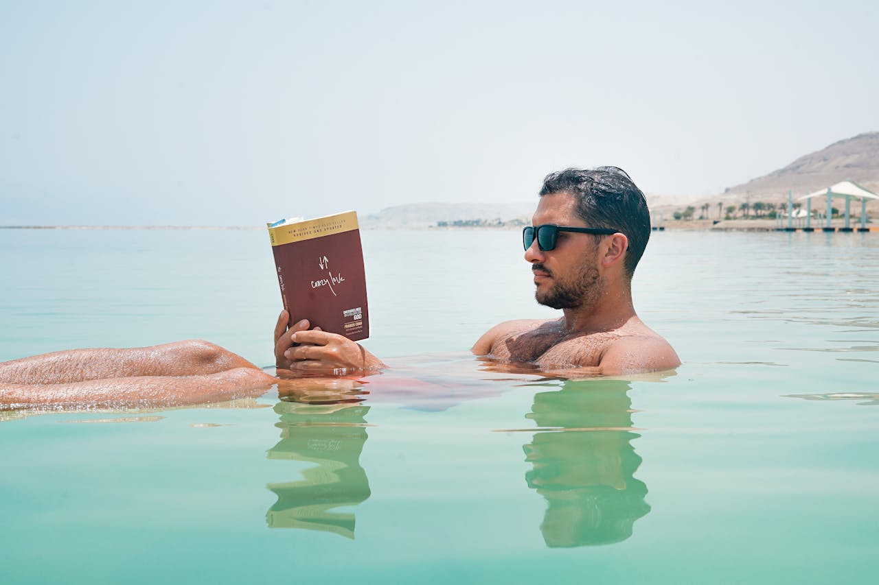 Relaxing man reading a book while floating on the Dead Sea under bright sunlight.